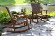 Load image into Gallery viewer, Two wooden rocking chairs on a stone patio with a garden and pond in the background.