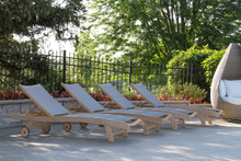 Load image into Gallery viewer, Row of wooden lounge chairs on a patio with trees and flowers