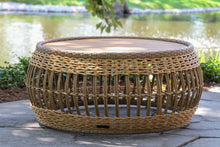Load image into Gallery viewer, Wicker ottoman on a stone patio with a blurred background of water and greenery
