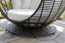 Load image into Gallery viewer, Black wicker chair with white cushion on a stone patio