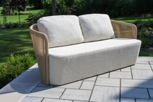 Load image into Gallery viewer, Outdoor sofa with beige cushions on a patio area with greenery in the background