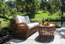 Load image into Gallery viewer, Outdoor patio set with wicker furniture and a small table by a pond.