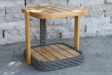Load image into Gallery viewer, Wooden side table with woven base against a stone wall.