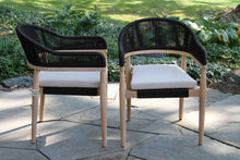 Load image into Gallery viewer, Two black and beige chairs on a stone patio with greenery in the background
