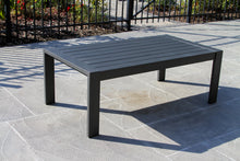 Load image into Gallery viewer, Gray outdoor table on a stone patio with a black metal fence in the background
