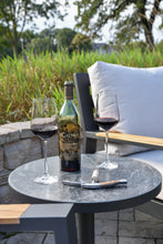 Load image into Gallery viewer, Wine bottle and glasses on a table outdoors with grass and trees in the background
