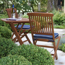 Load image into Gallery viewer, Wooden outdoor table and chairs with blue cushions in a garden setting
