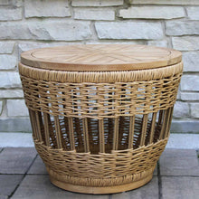 Load image into Gallery viewer, Wicker side table with wooden top against a stone wall.
