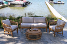Load image into Gallery viewer, Outdoor patio set with wicker furniture and cushions by a waterfront.
