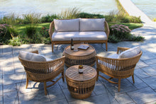 Load image into Gallery viewer, Outdoor patio set with wicker furniture on a stone patio by a body of water.
