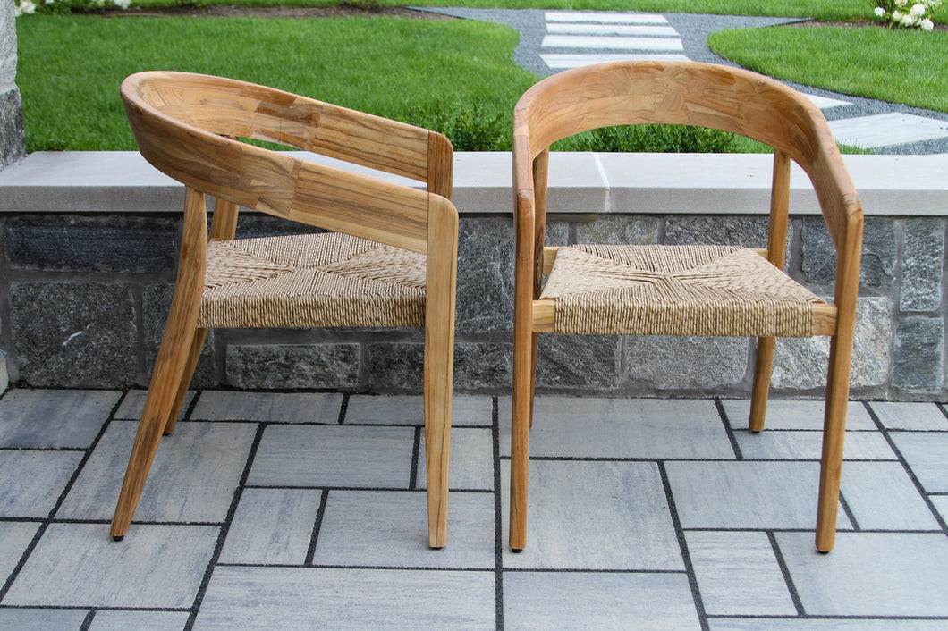 Two wooden chairs with woven seats on a stone patio.